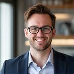 Portret Mgr Tomasza Nowaka, sympatycznego mężczyzny w okularach w średnim wieku na niebieskim tle